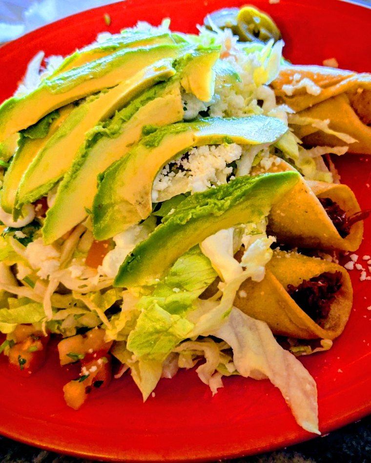 Crispy flautas topped with avocado, lettuce and crema on a red plate