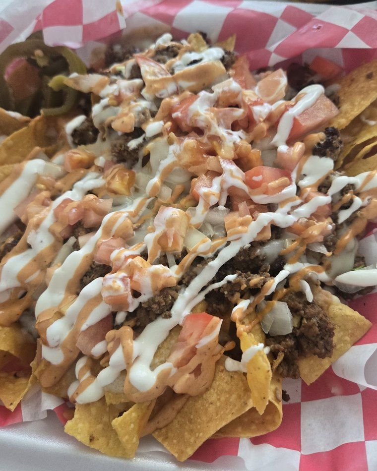 Loaded nachos — tortilla chips piled with meat, beans, pico and a crema-and-salsa drizzle in a red basket