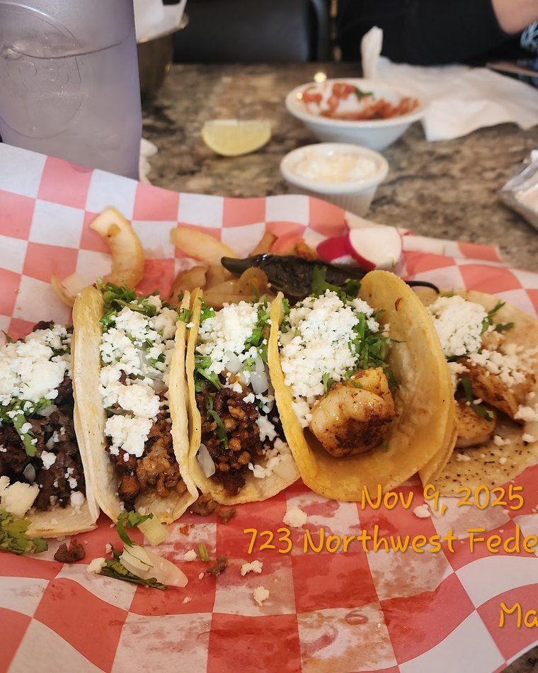 Three soft corn street tacos in a basket, topped with cilantro, onion and queso fresco