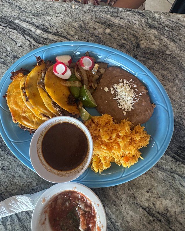 Birria tacos with a cup of consommé on a blue plate