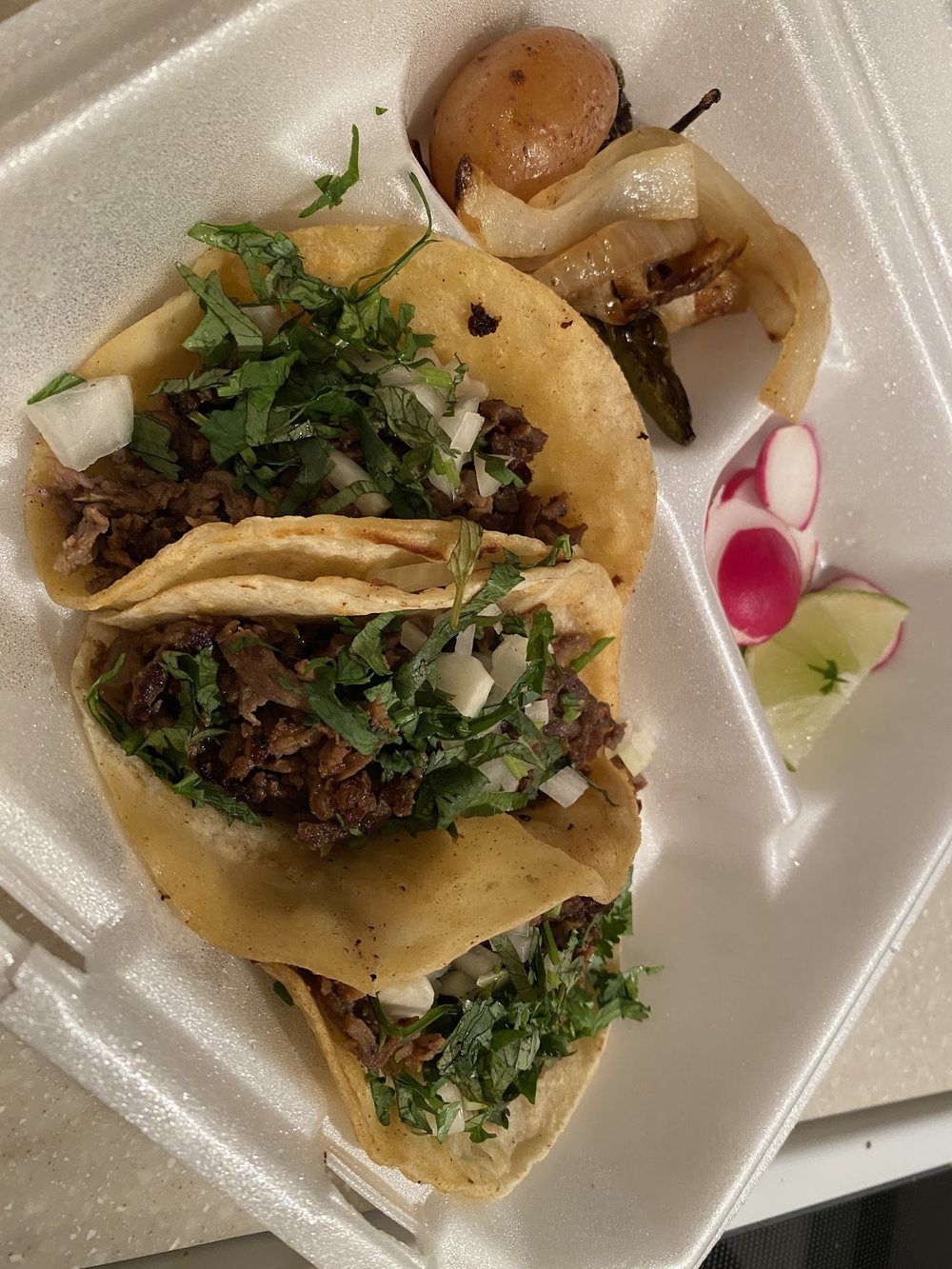 Soft corn street tacos topped with cilantro, onion and a wedge of lime on a plate