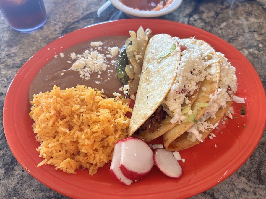 A combo plate with a soft taco, yellow rice and refried beans on a red plate
