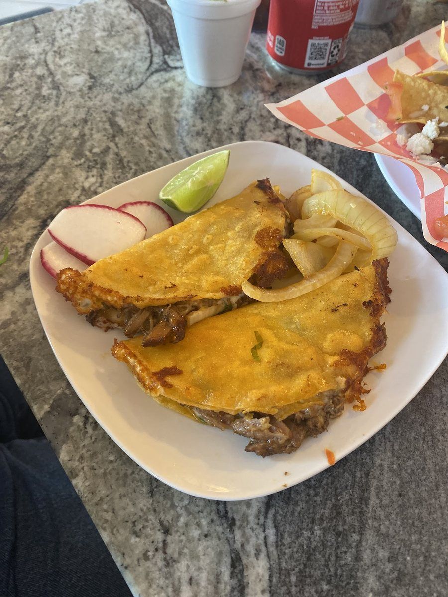 Two crisp golden fried tacos with radish and lime on a tray
