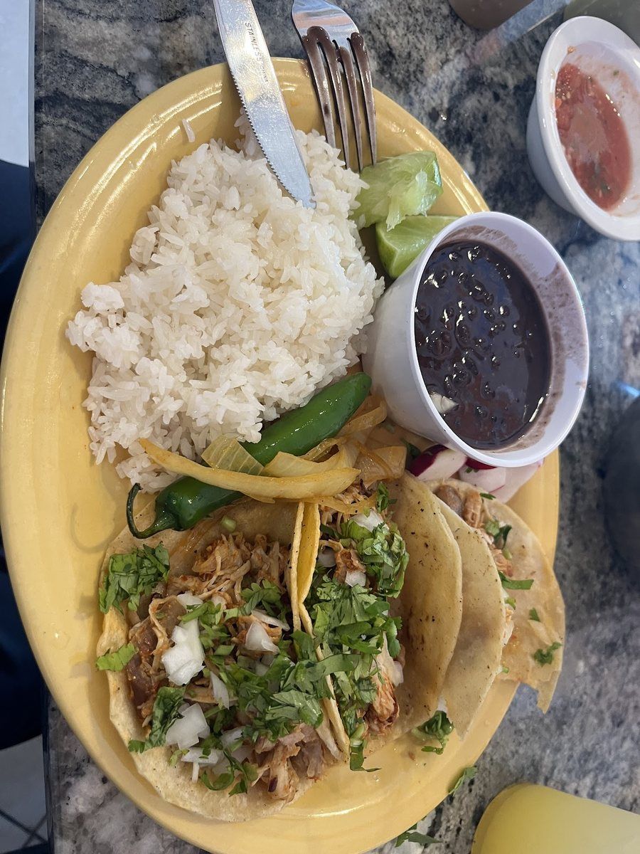 A taco plate with white rice, black beans and sliced avocado on a yellow plate