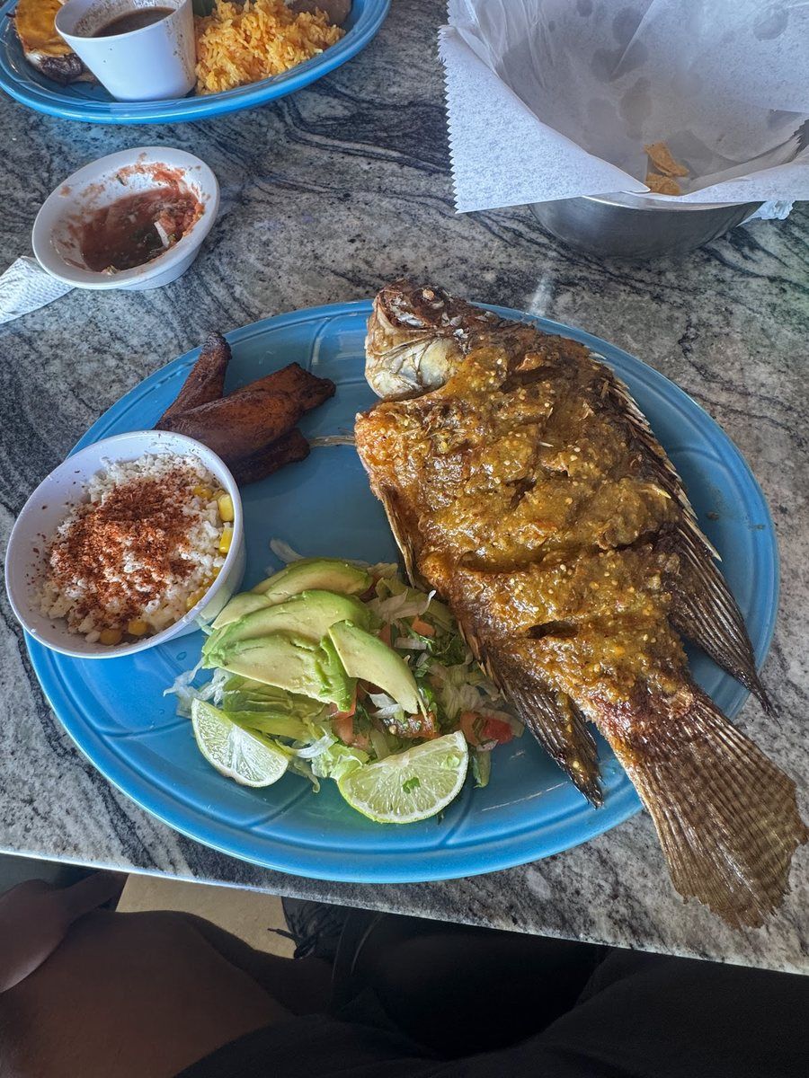 Whole fried mojarra with sliced avocado on a blue plate