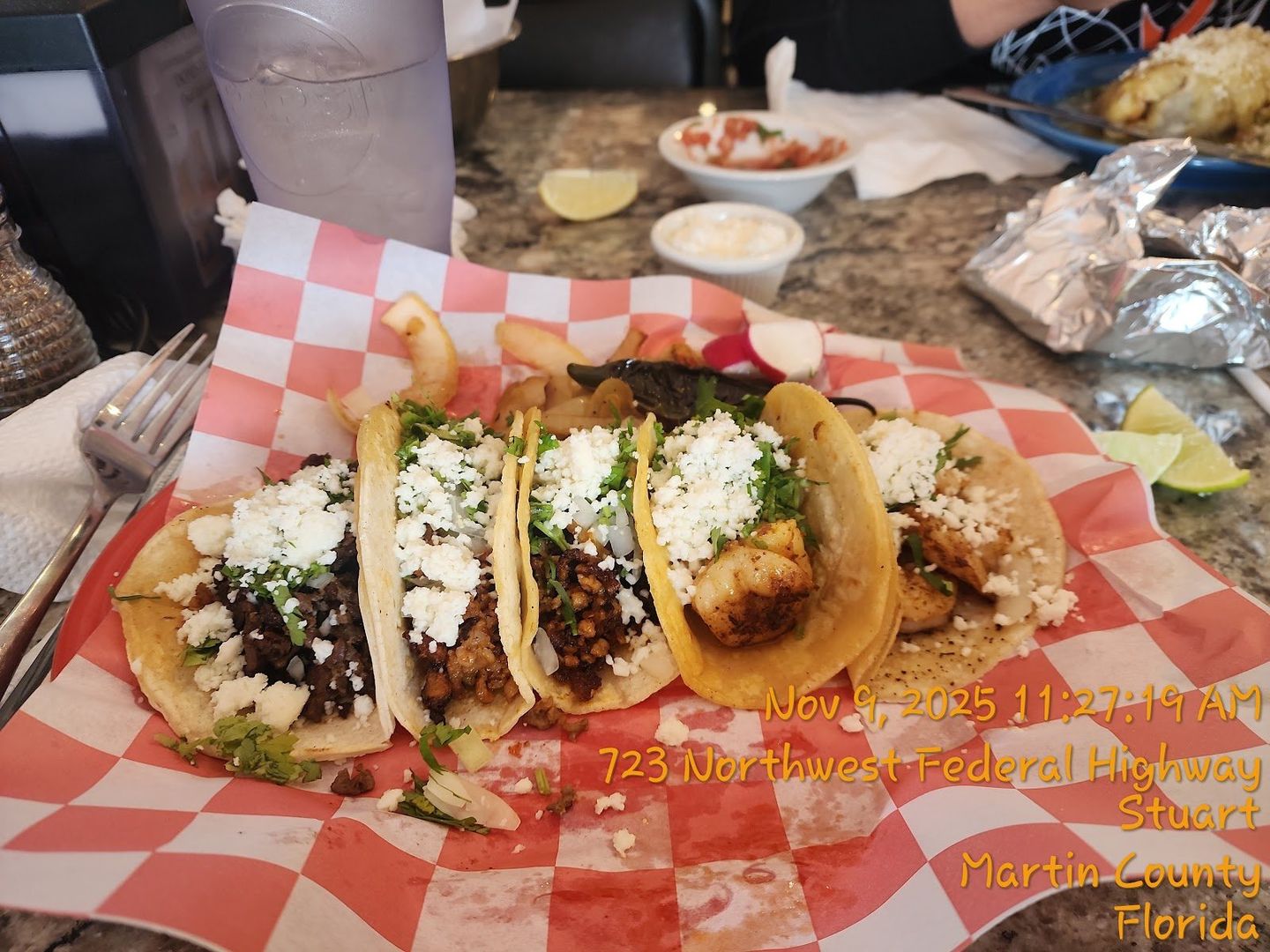 A basket of fresh street tacos on soft corn tortillas, topped with cilantro and onion, with lime on the side
