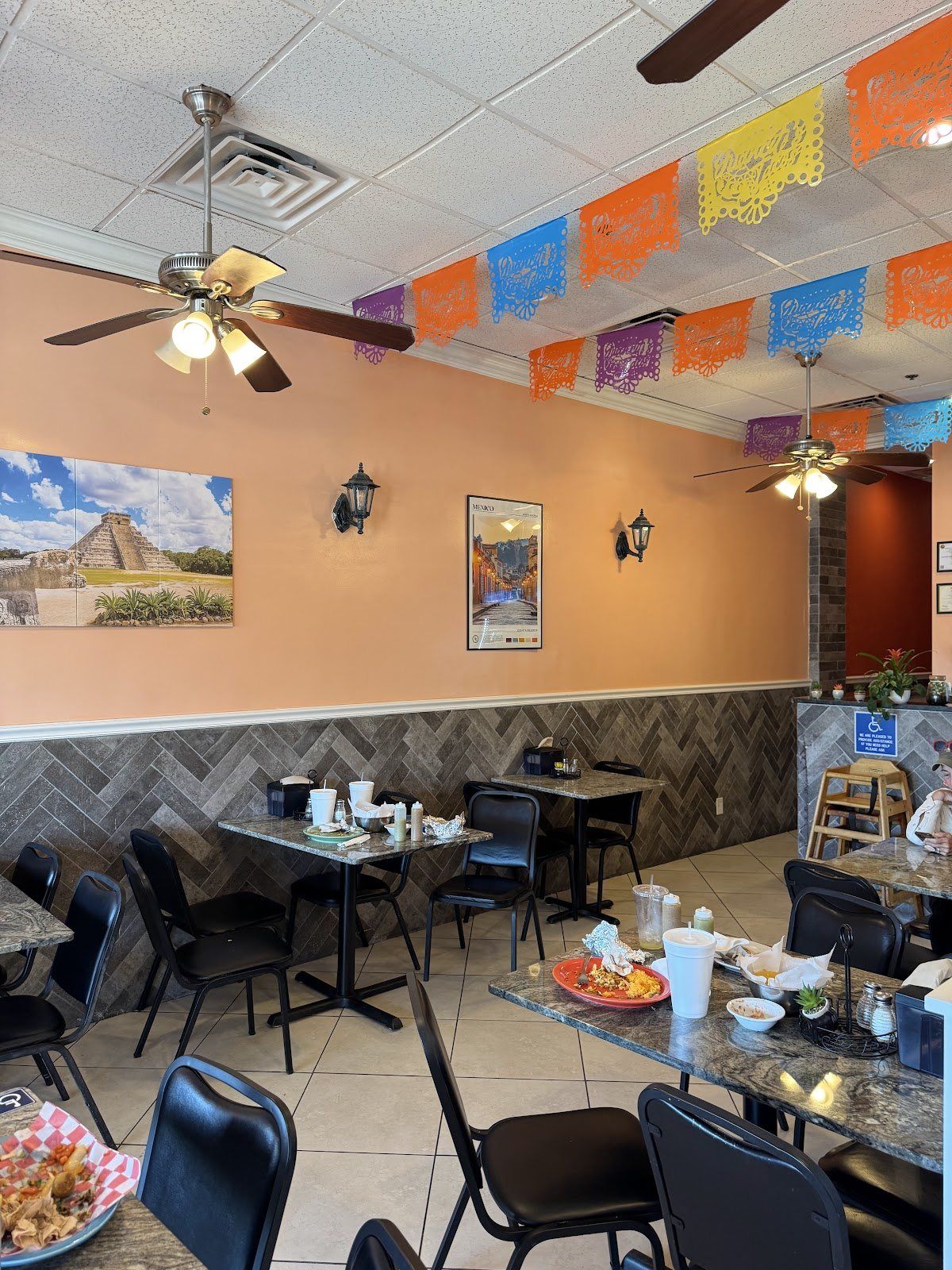 The festive dining room — warm terracotta walls, papel-picado banners strung across the ceiling and a desert mural