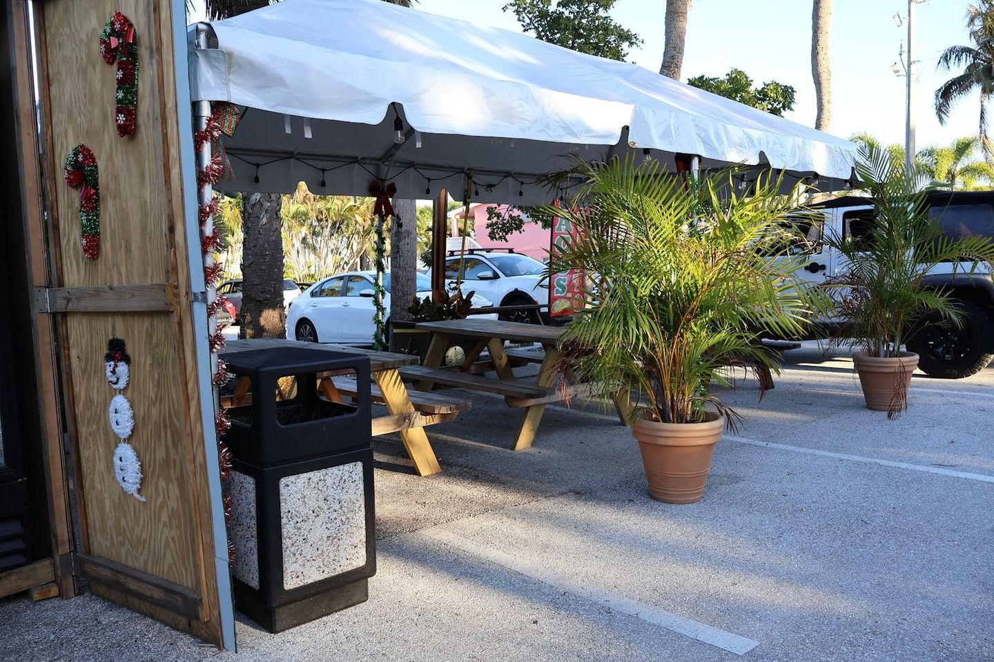 The covered outdoor patio with picnic tables and potted palms