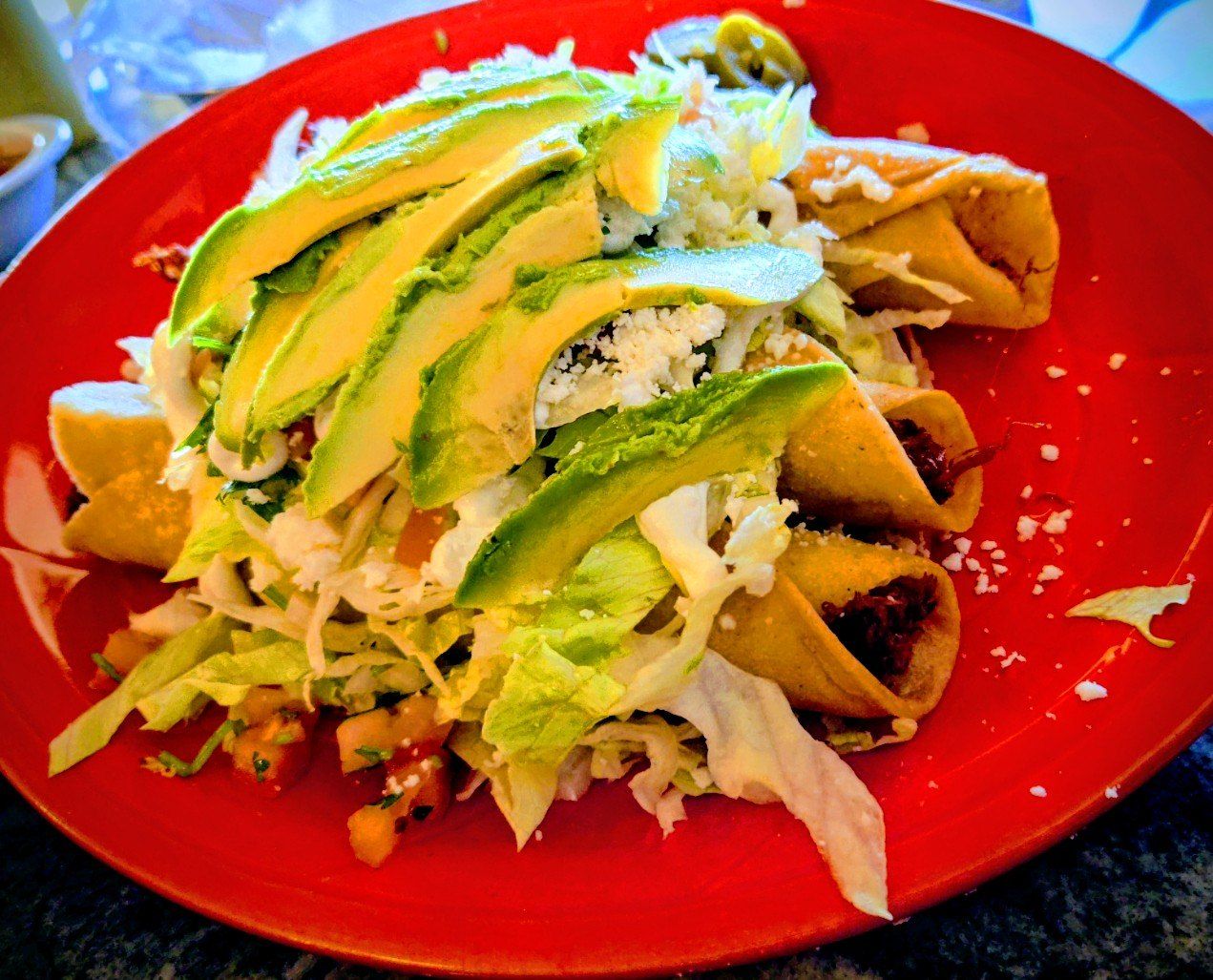 Crispy flautas topped with avocado, lettuce and crema on a red plate