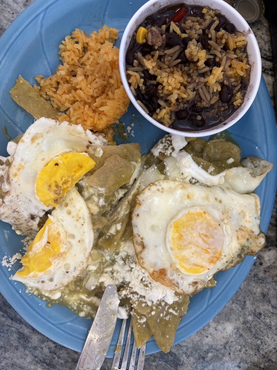 Breakfast plate — two fried eggs over green chilaquiles with rice and refried beans on a blue plate