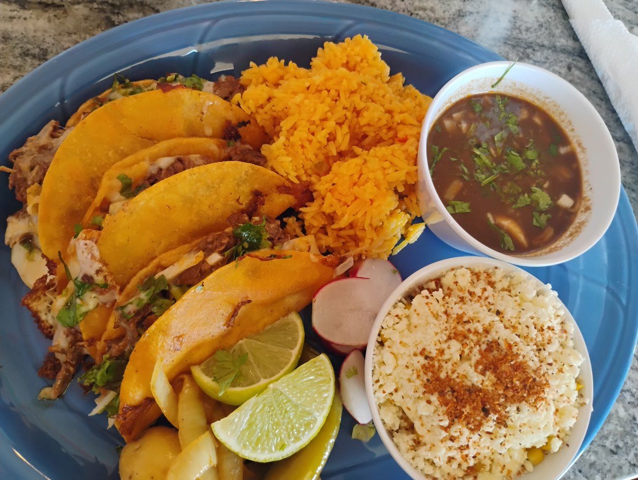 Birria tacos with rice, consommé and a cup of horchata on a blue plate